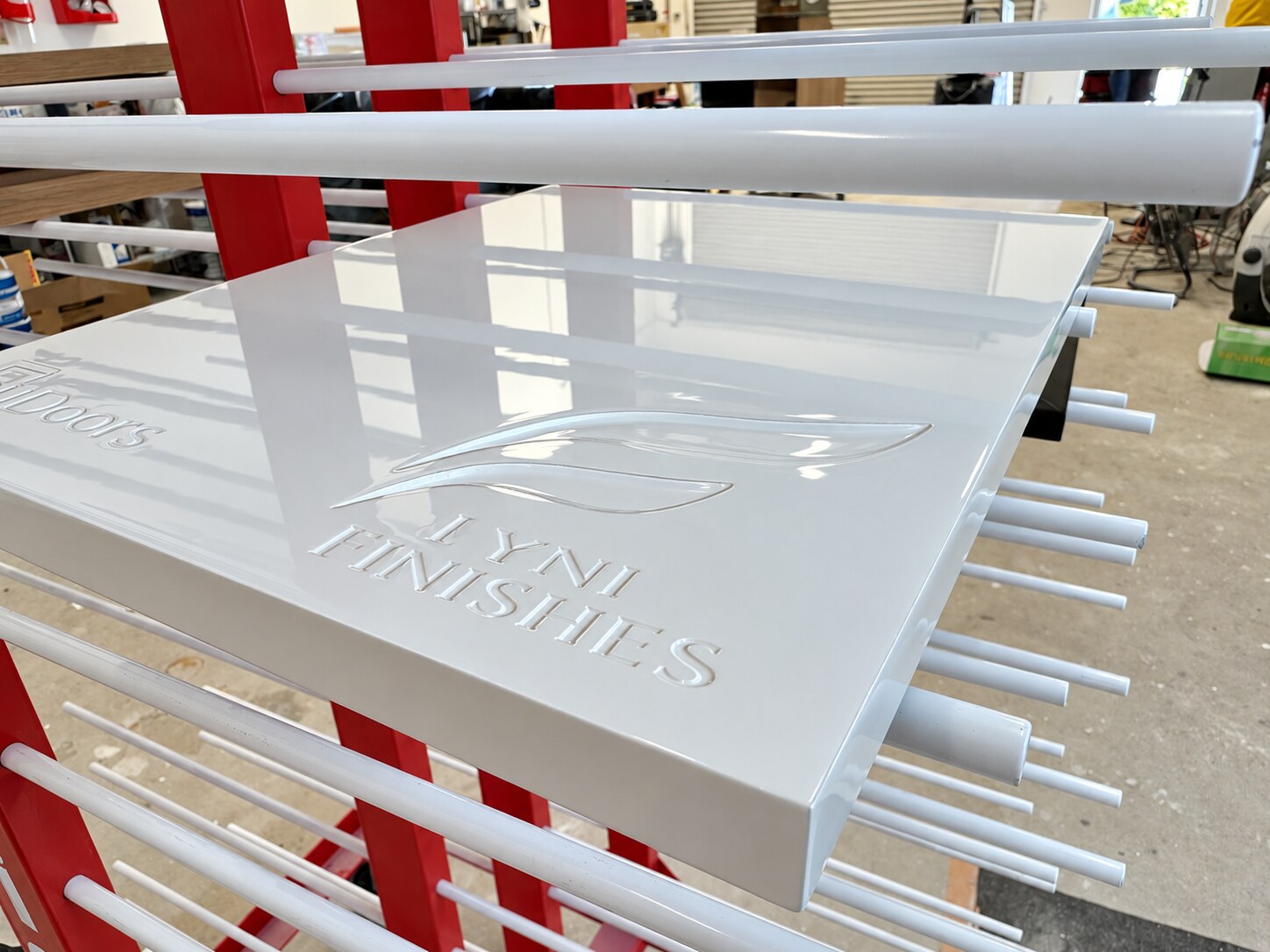 High-gloss sprayed Fyne Finishes sample panel curing on a finishing rack