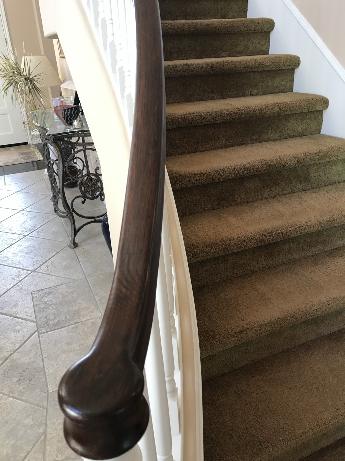 Close view of a stained wood handrail with visible grain beside white balusters